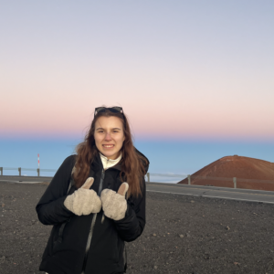 Profile picture of Sonja giving a thumbs up infront of a scenic view.